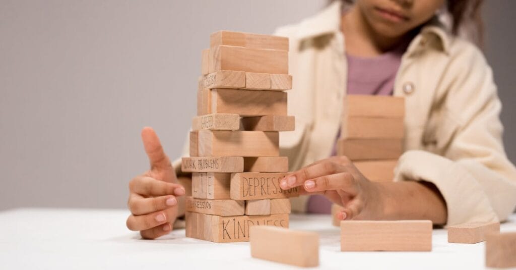 A child thoughtfully stacks wooden blocks with words like 'depression' and 'kindness.'