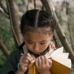 Young girl scout in forest taking notes in a notebook.