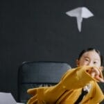 A playful scene of a young girl in an office throwing a paper airplane, featuring a globe and desk lamp.