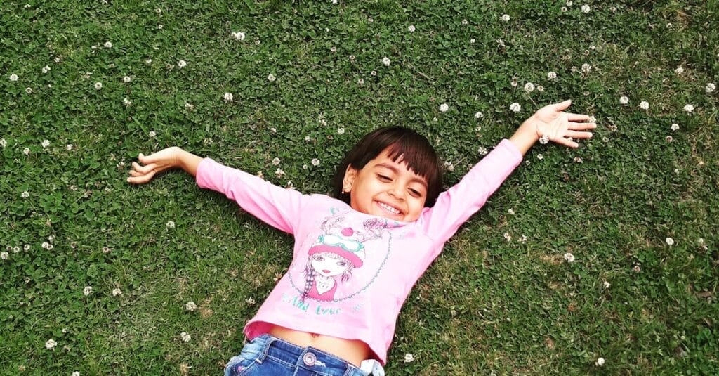 Happy child enjoying a carefree moment lying on grass, arms wide open.