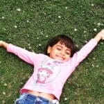 Happy child enjoying a carefree moment lying on grass, arms wide open.