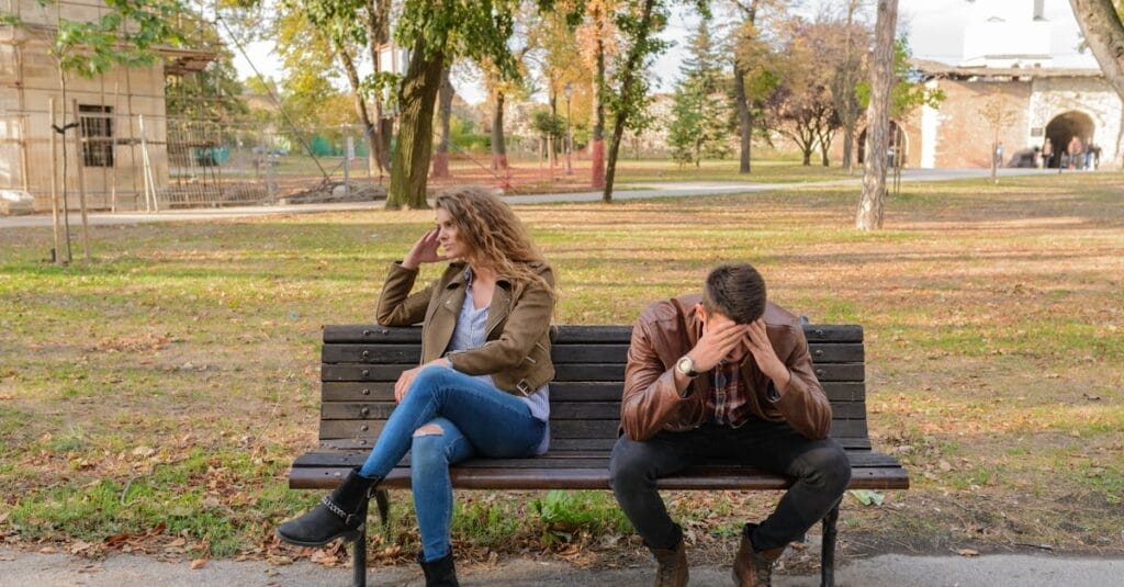 An upset couple seated on a park bench, expressing frustration during an autumn day.