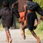 Three children running barefoot on a rural path, showcasing friendship and joy in a natural setting.