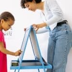A child and teacher interact at a chalkboard, fostering education and creativity.