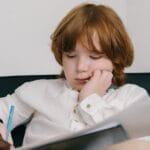 Young boy with freckles focused on drawing during an education session indoors.