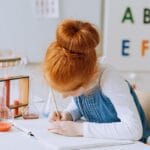 A young girl writing in a notebook, surrounded by test tubes, learning about science in a classroom.